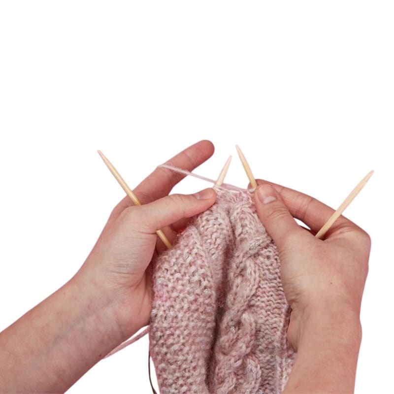 Hände stricken einen rosa Kabelmuster-Pullover mit Holzstricknadeln